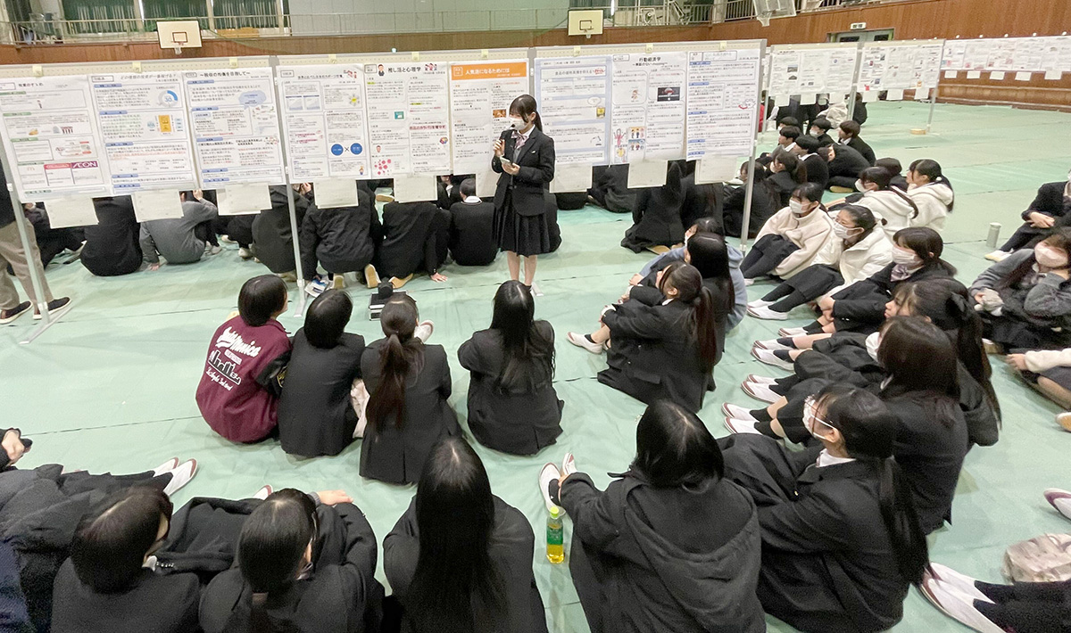 体育館のような広い室内で、生徒たちがポスター発表を行っている様子の写真。