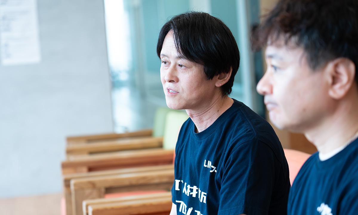柴崎さんと水上さんのバストショット。柴崎さんは黒い「LINEヤフー IT人材育成プロジェクト」と書かれたTシャツを着て、やや前を見つめながら落ち着いた表情で話を聞いている様子。