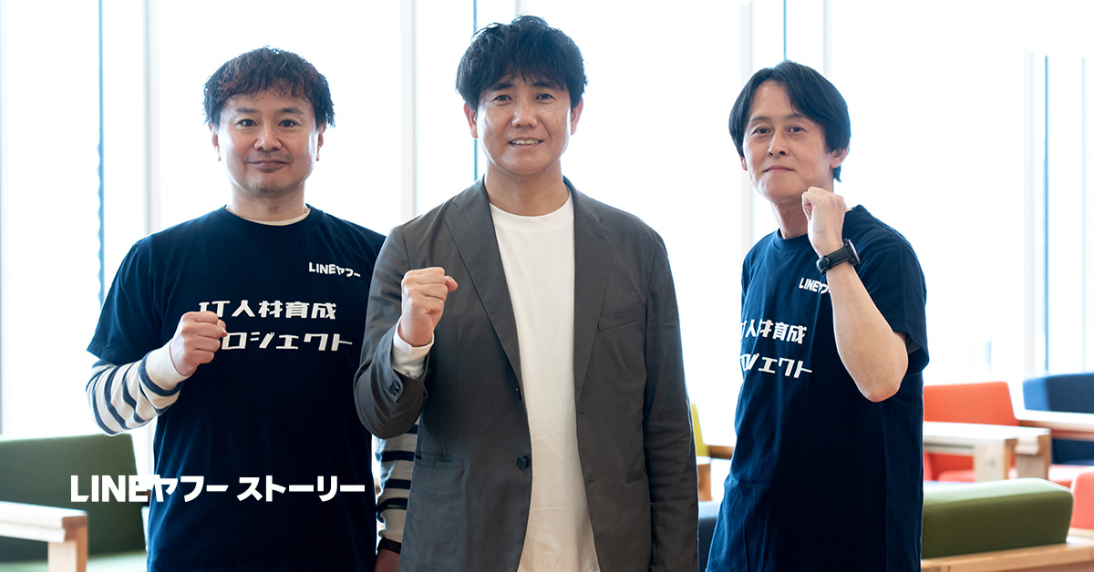 3人の男性、水上、生井さん、柴崎が横一列に並び、室内で拳を軽く握ってポーズを取っている写真。左右の2人のTシャツには「LINEヤフー」および「IT人材育成プロジェクト」と書かれている。