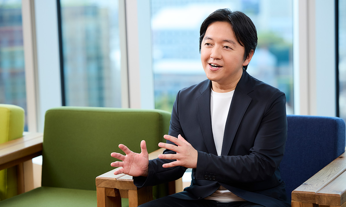 男性が手を使って説明をしている場面です。リラックスした表情で、背景には都会のビル群が広がっています。