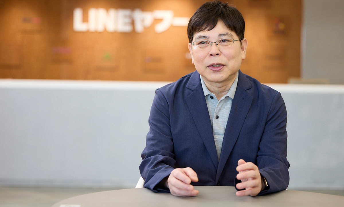 テーブルに座った男性が、手を使って説明をしています。背後には「LINEヤフー」のロゴがあり、オフィスの一角が見えます。