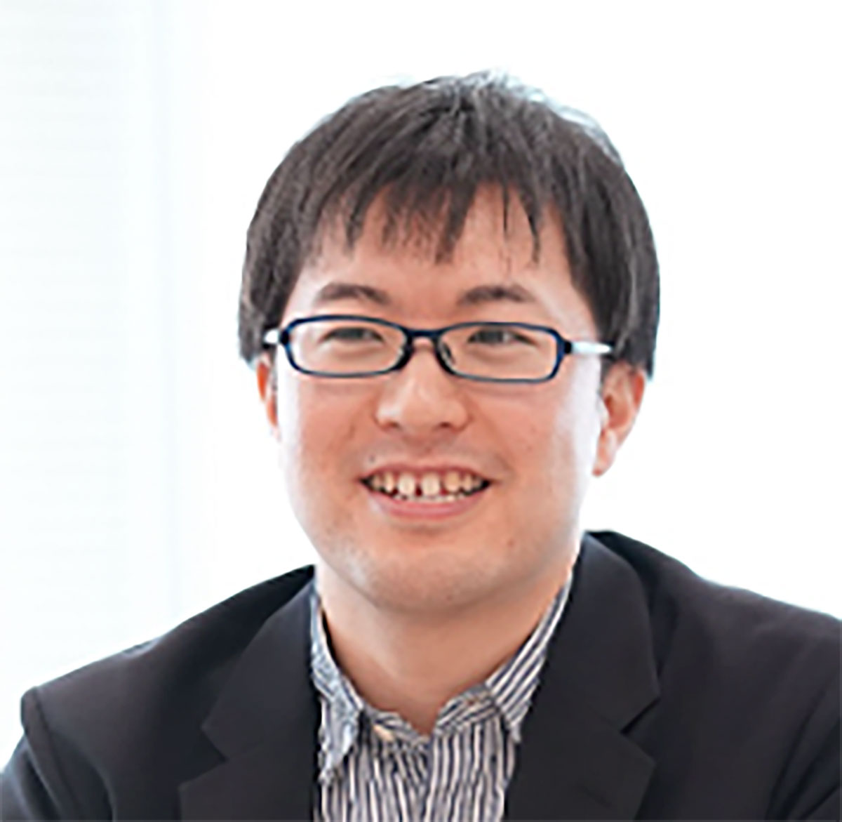 笑顔の圓井のクローズアップ。眼鏡をかけ、ストライプのシャツとジャケットを着用しています。