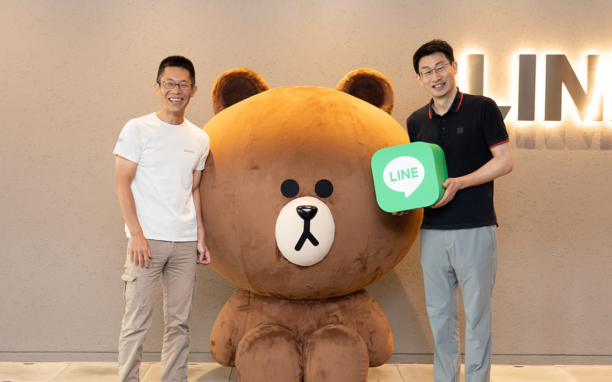 朝井と慎が大型のLINEキャラクター「ブラウン」と並んで立っている写真である。
