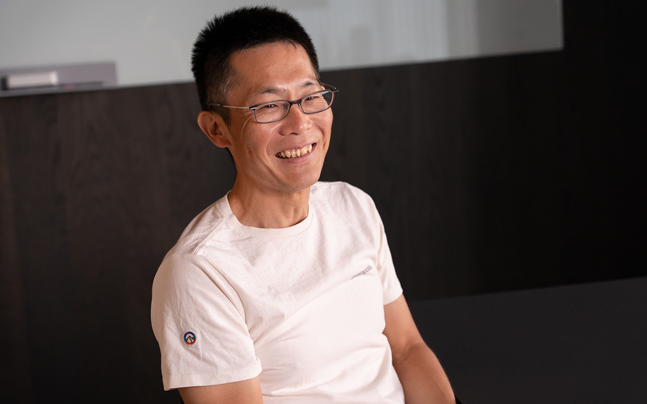 朝井が体をやや斜めに向けながらリラックスした姿勢で椅子に座り、笑顔で会話している様子
