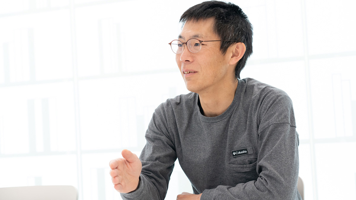 LINEの責任者である朝井が写っている写真。明るい室内でテーブルに向かって座り、体をやや前に傾けながら片手を前に出して話している様子。