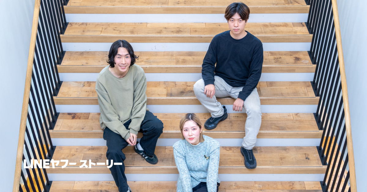 木製の階段に三人が座っている写真。中央下に金髪ボブの女性、左右上段に男性二人が座り、全員カジュアルな服装でカメラを見ている。左下に「LINEヤフーストーリー」と白文字がある