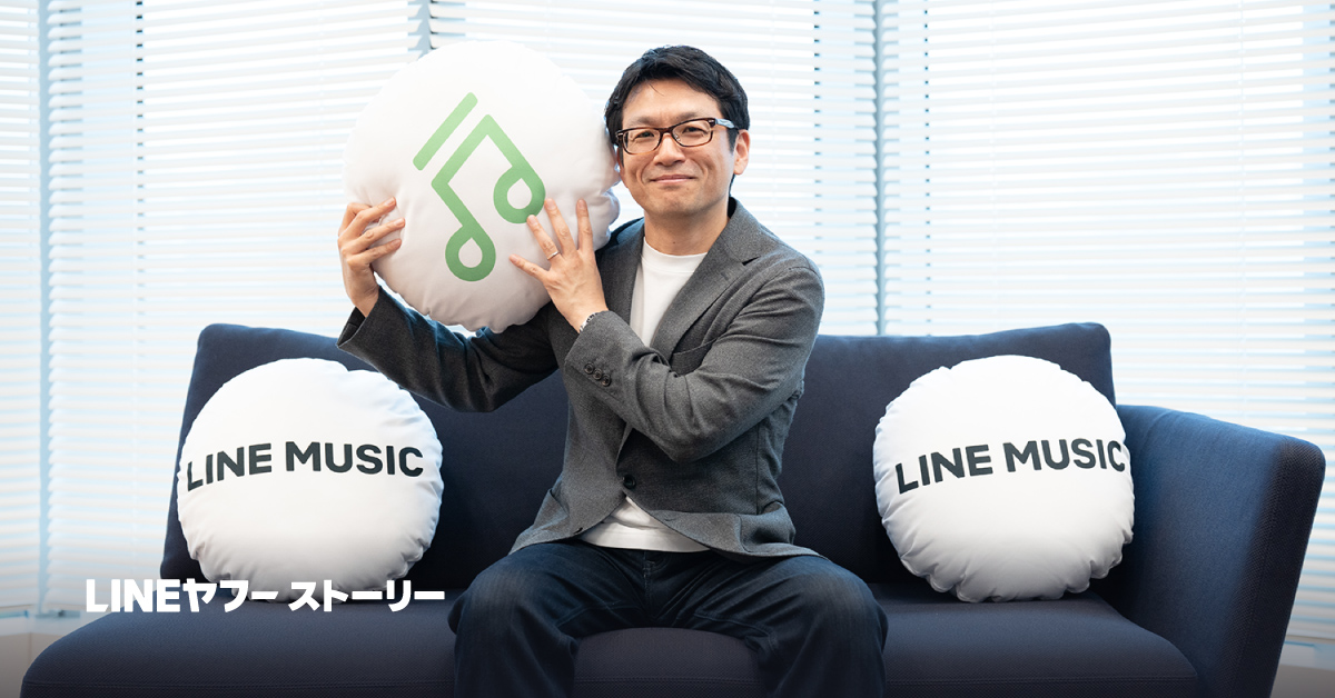 LINE MUSIC取締役COO高橋明彦の写真。LINE MUSICのロゴ入りクッションを持ち、ソファに座っています。