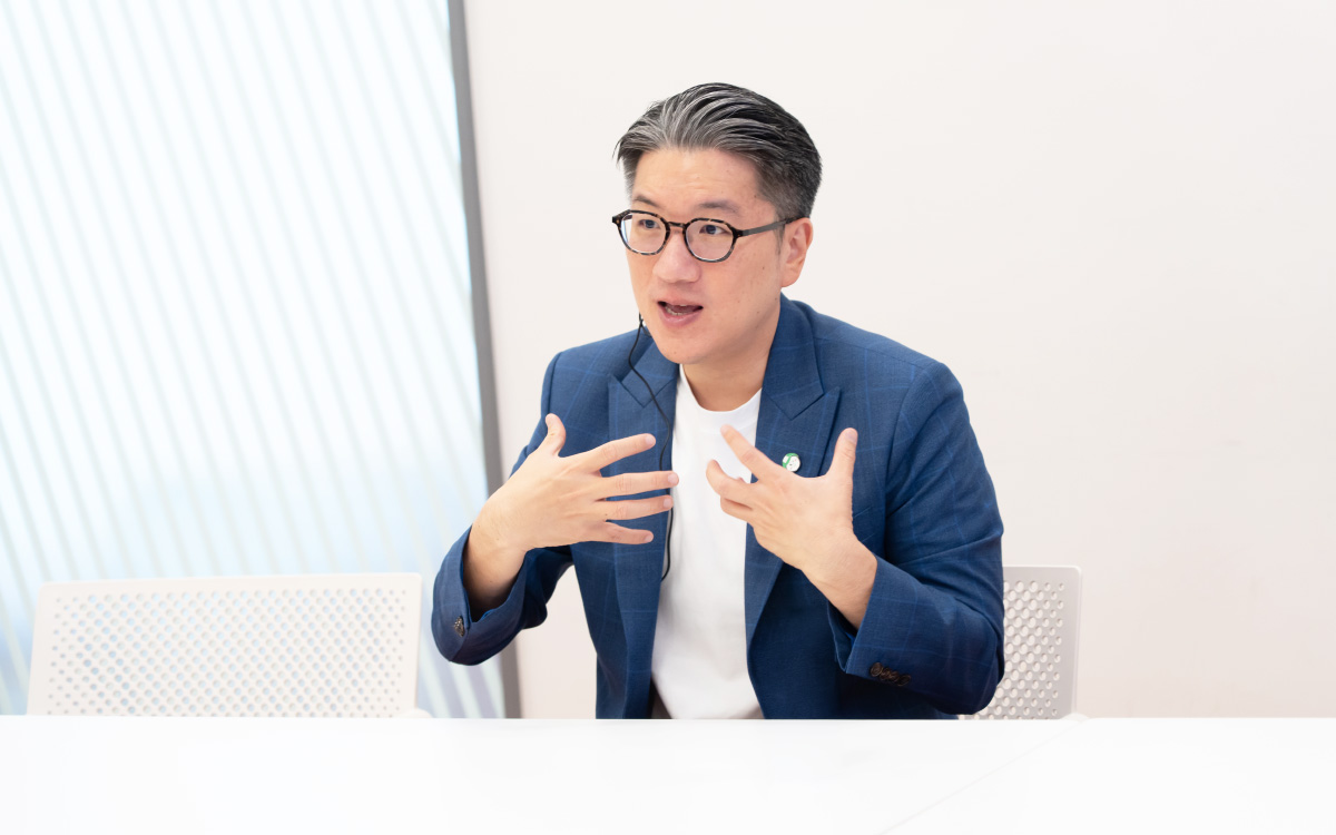 Yod Chinsupakulのバストショット。椅子に座り、両手を胸元に上げて指を広げながら、自身の考えを強調するように話している。