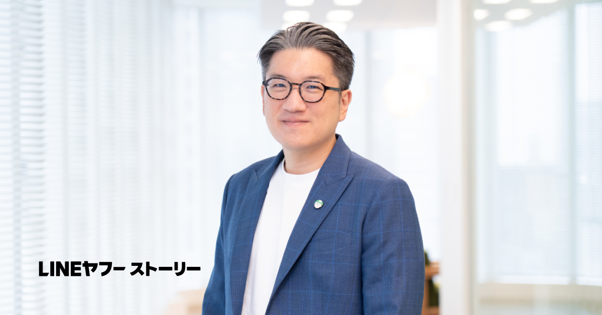 Yod Chinsupakulのバストショット。グレーがかった黒髪を後ろに整え、黒縁の丸眼鏡をかけている。穏やかな笑みを浮かべ、やや斜めに体を向けて立っている。背景は明るいオフィス空間で、左下には「LINEヤフーストーリー」という文字が表示されている。