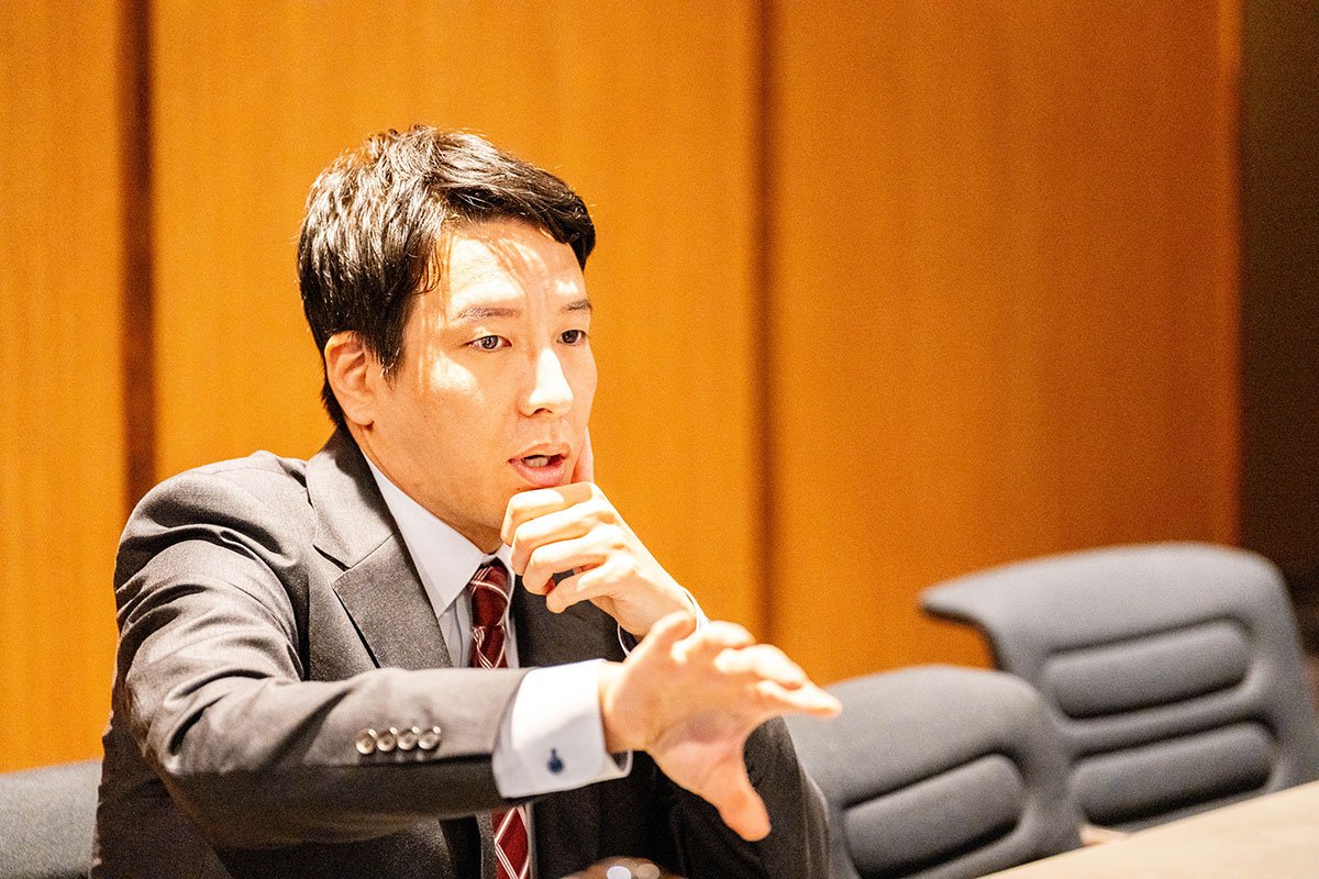 会議室で金剛洙さんが片手を前に伸ばしながら説明している写真。スーツ姿で身振りを交えて話している