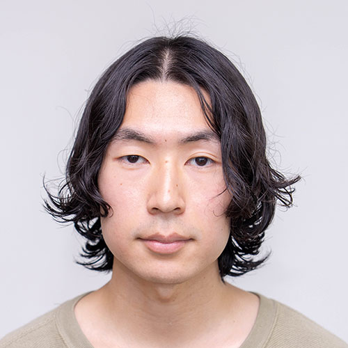 グレー背景で正面を見つめる松浦のバストショット。肩にかかる黒髪を中央分けにし、ベージュのトップスを着用して落ち着いた表情を浮かべている