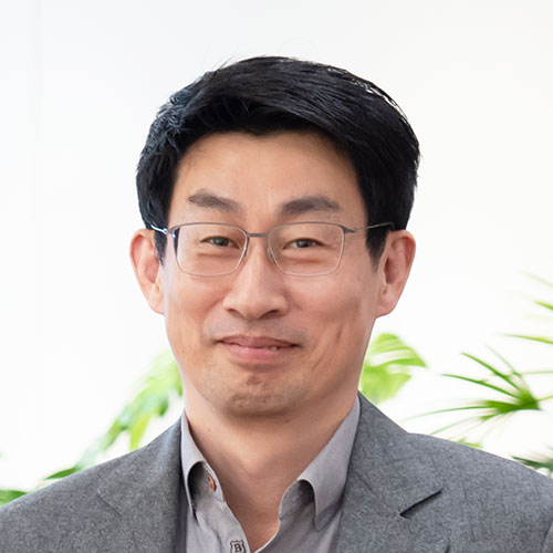 グレージャケットを着たCPO慎の顔のクローズアップ。短髪にメガネをかけ、柔らかな表情で正面を見ている