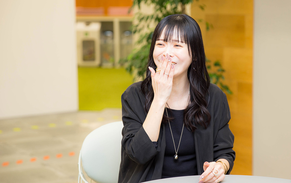 菅沼が笑いながら右手で口元を軽く押さえている写真。