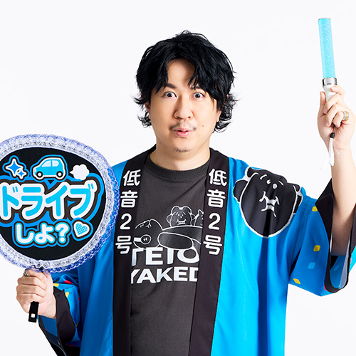  青い法被を着た男性が「ドライブしよ？」と書かれたうちわとサイリウムを持ち、楽しそうにしています。