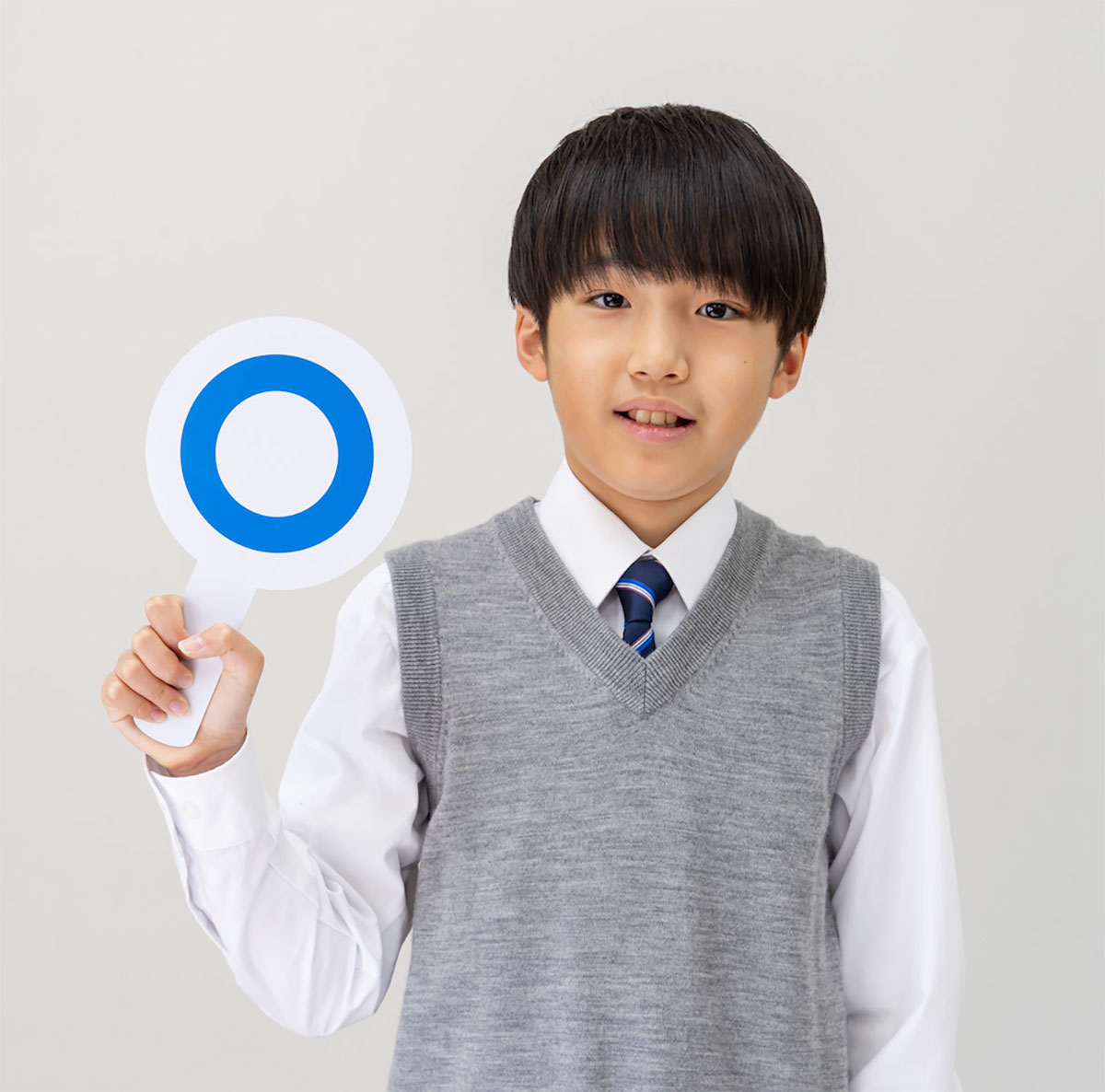 グレーのベストを着た少年が、青い丸印の札を持っている姿です。彼はほほ笑んでいます