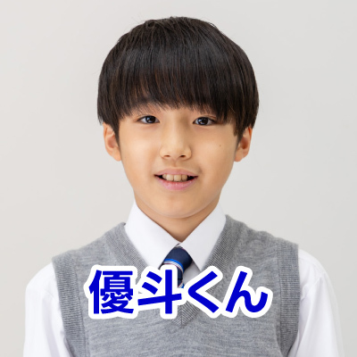 白いシャツとグレーのベストを着た若い男の子がほほ笑んでいる姿です