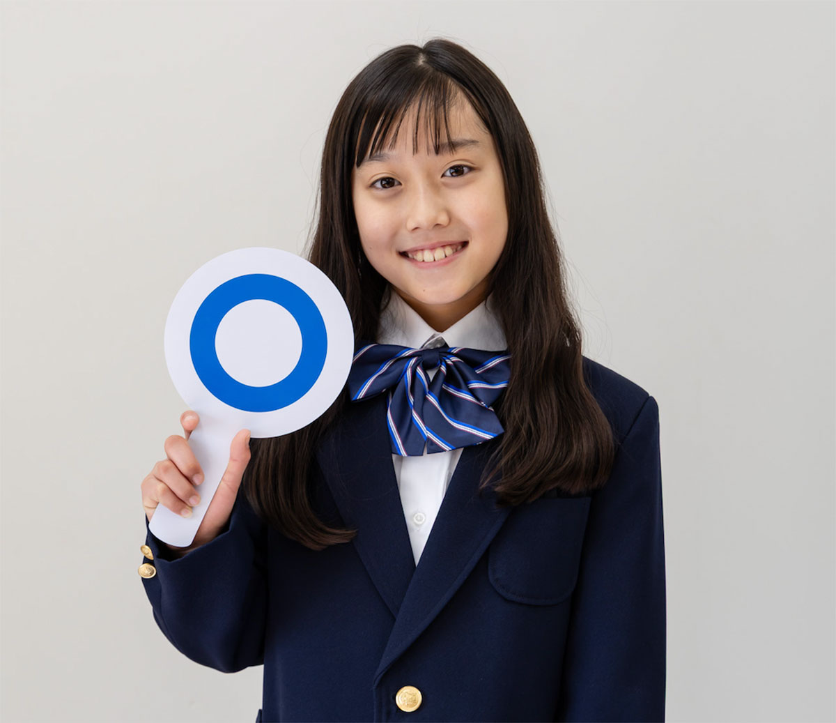 青い制服を着た少女が、青い丸印の札を持ってほほ笑んでいる様子です