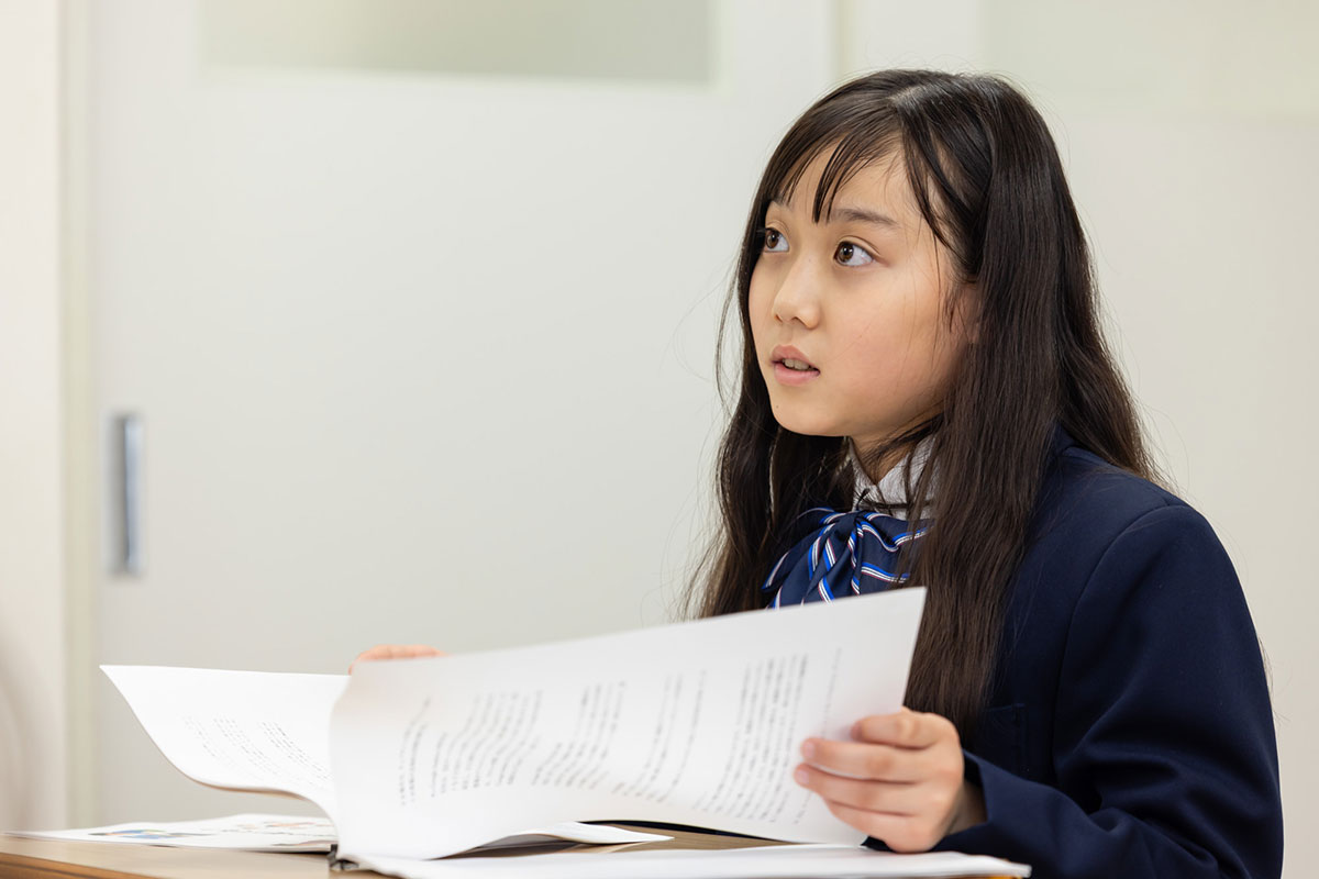 少女が教科書を見ながら驚いた表情をしている様子です。彼女は何かに気付いたようです