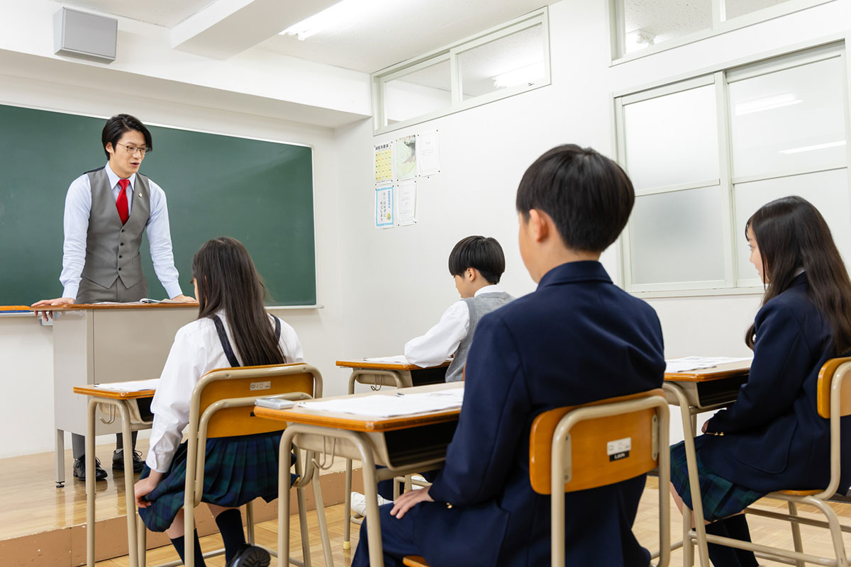 教室で生徒たちが前を見て授業を受けている様子です。男の子と女の子が真剣に話を聞いています