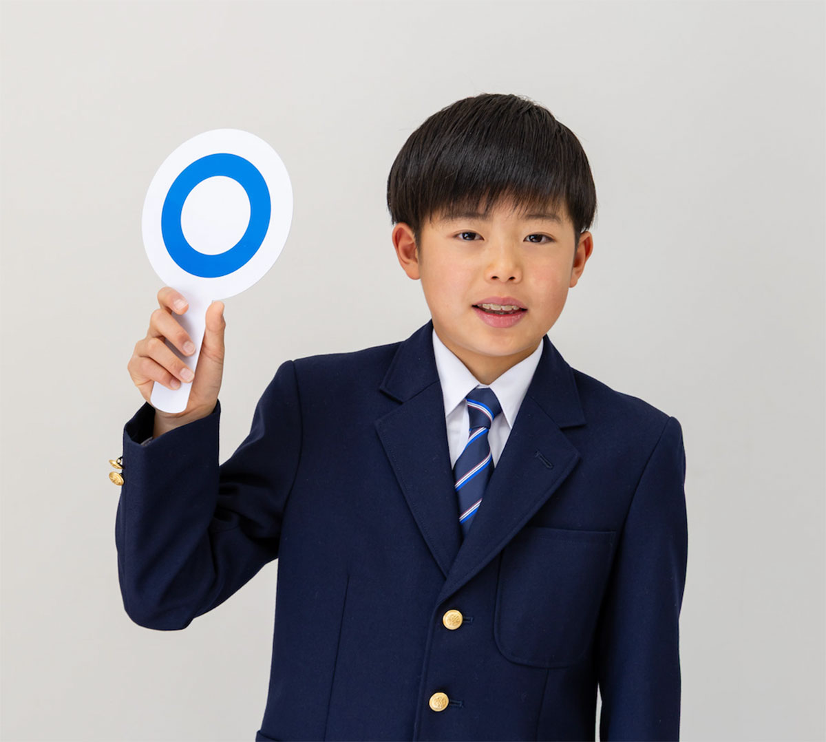 青い制服を着た少年が、青い丸印の札を持っている姿です。彼はほほ笑んでいます