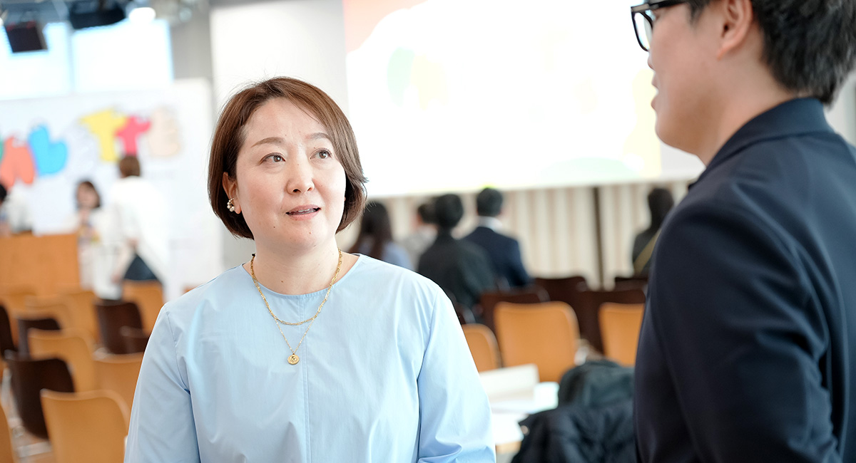 寺澤がイベント会場で番場と会話している様子。背景にはカラフルな「PALETTE」の文字が見えます。