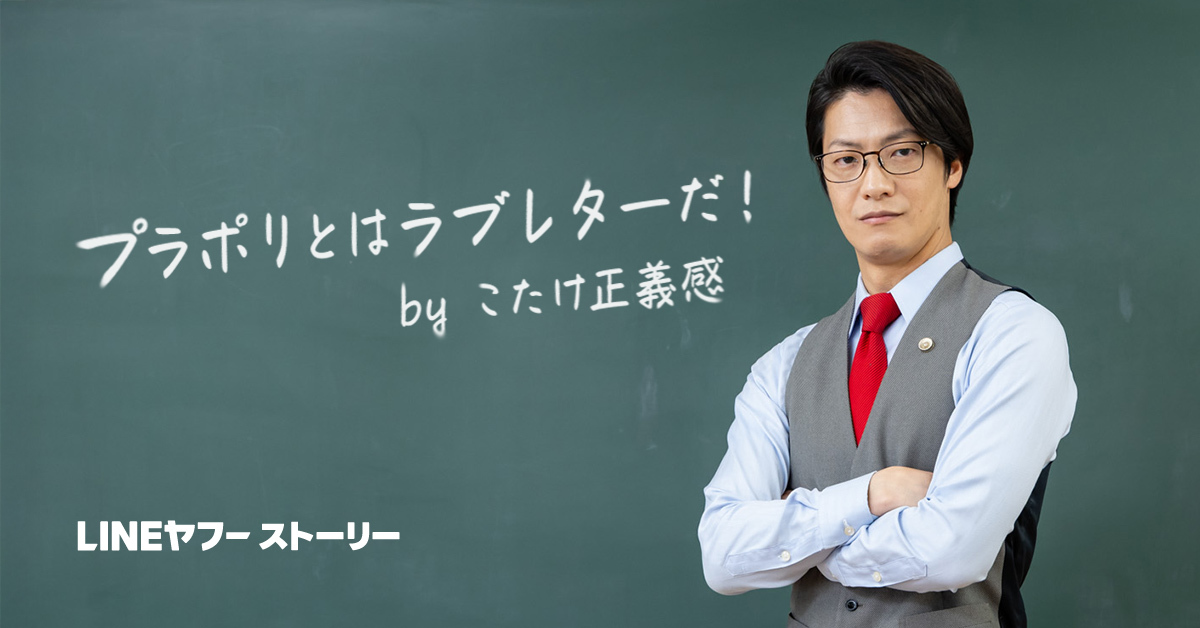 黒板の前に立つ眼鏡をかけた男性・こたけ正義感さんが、腕を組んでいる姿です。黒板には日本語の文字「プラポリとはラブレターだ」が書かれています