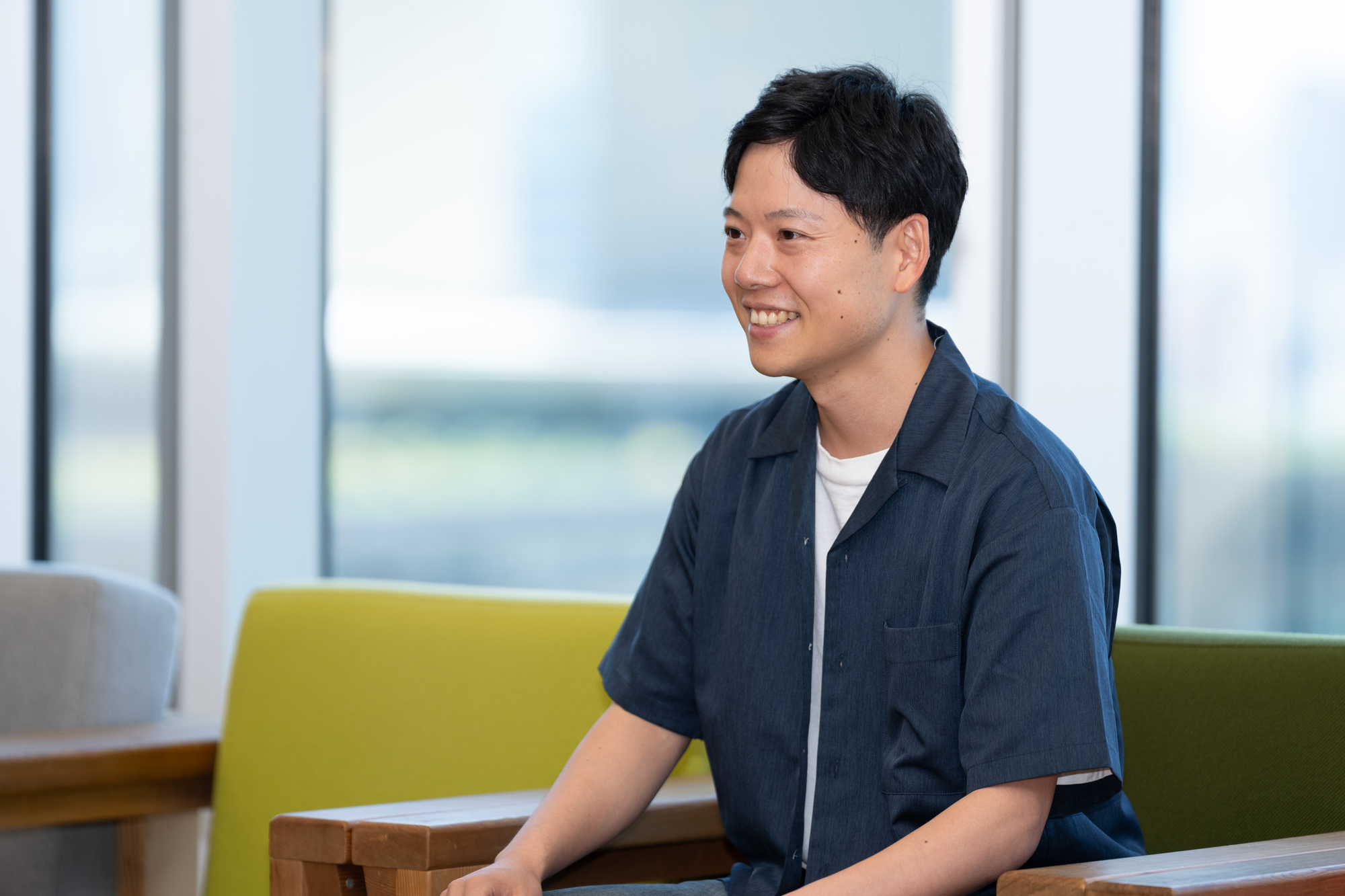 明るい光が差し込むなか、緑色のソファに腰かけて材木がインタビューに答えている