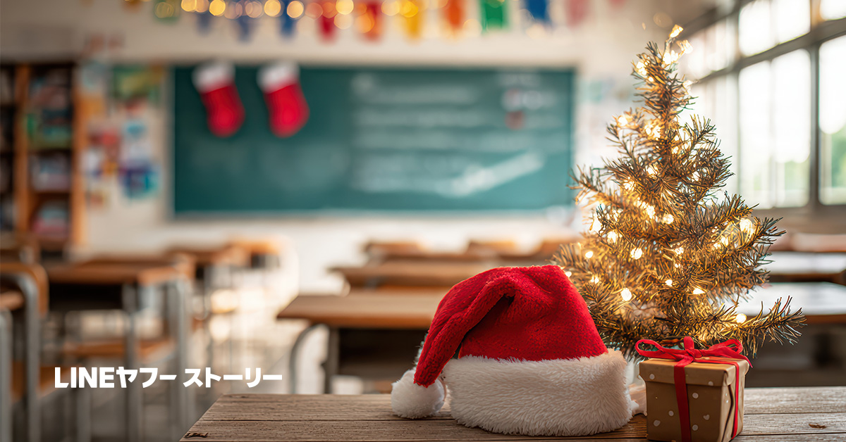 教室の中を背景に、小さなクリスマスツリーとサンタ帽、リボン付きのプレゼント箱が机の上に置かれている。