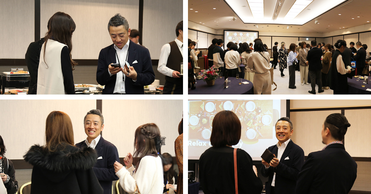 ビジネスイベントで、多くの人々が集まり交流しています。男性が参加者と会話している様子や、会場全体の賑やかな雰囲気が伝わります。