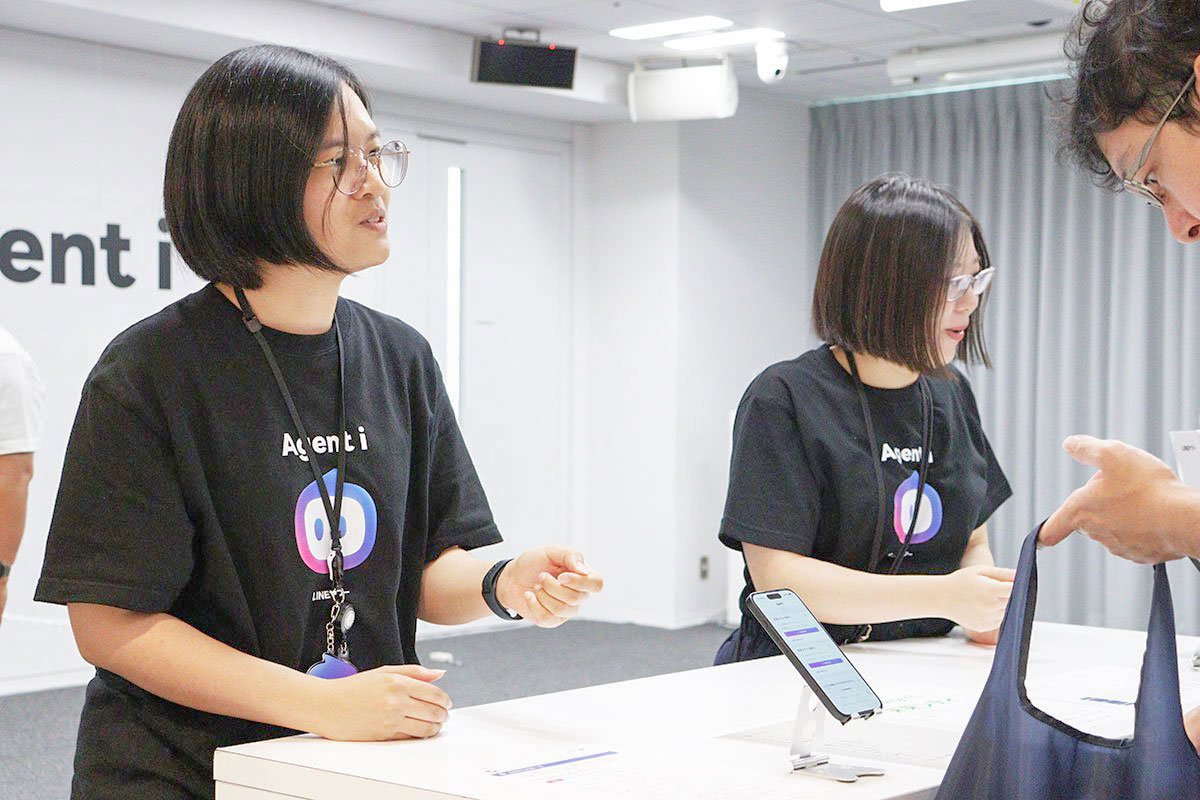 Agent iのTシャツを着たパリンと大石が、来場者にカレンダーエージェントを説明している写真