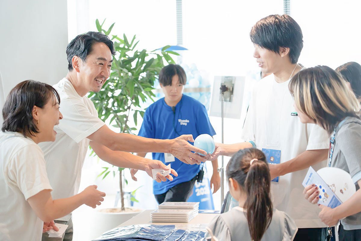 CEOの出澤剛と伊東由理が、巨大ガチャで家族連れのゲストに景品を手渡している写真