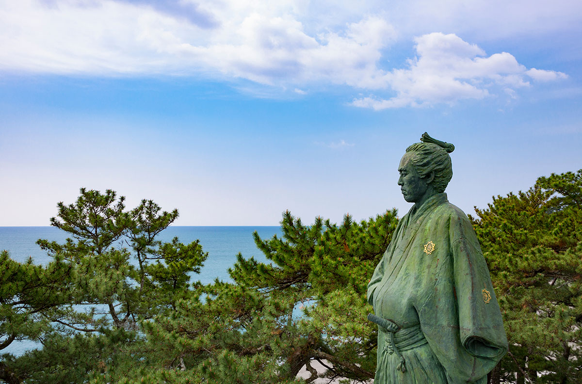 海を背にした武士像が松林の前に立つ。歴史を感じる表情と空の澄んだ青さが対照的で雄大な景色。