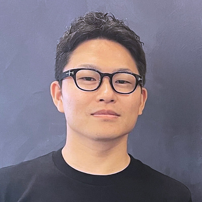 スーツを着た男性が腕を組み、街並みを背景にして立っている姿です。