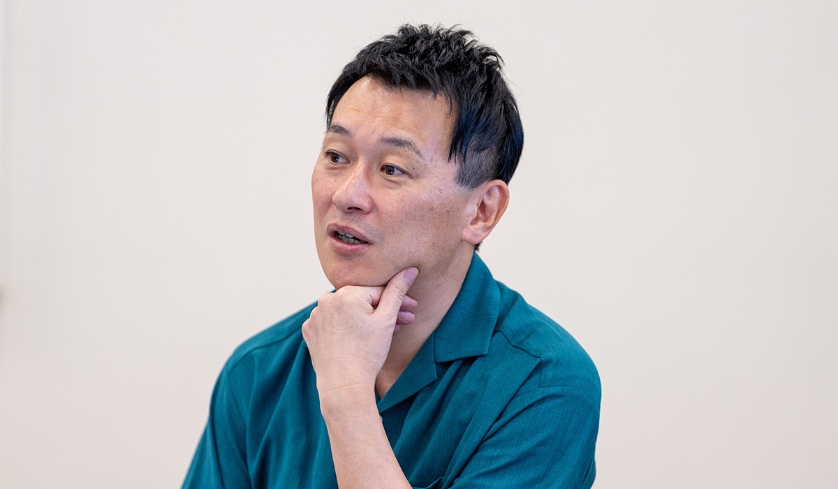 坂上さんがあごに手を当て、考えながら話をしている様子です。落ち着いた表情をしています。