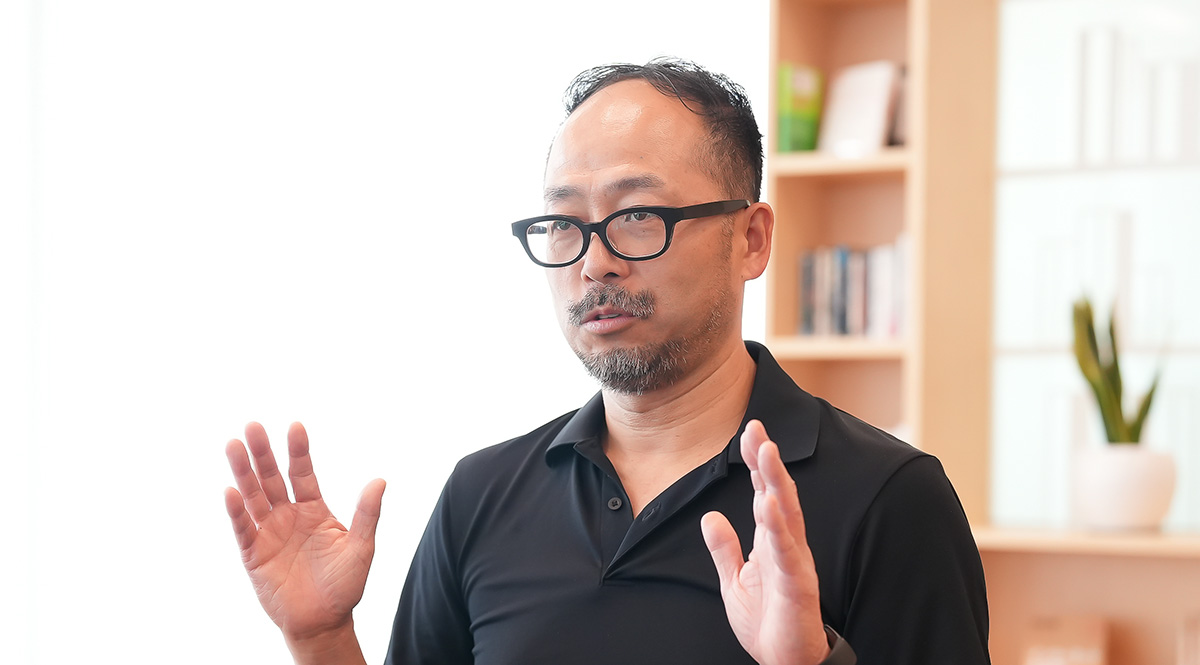黒い服を着太田が、手を広げて話をしている様子です。背景には本棚と植物が見え、明るい雰囲気です。