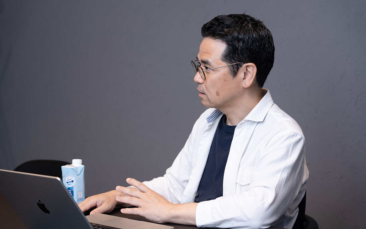 田中が右手をキーボード付近に置き、左手を軽く浮かせながら話している様子