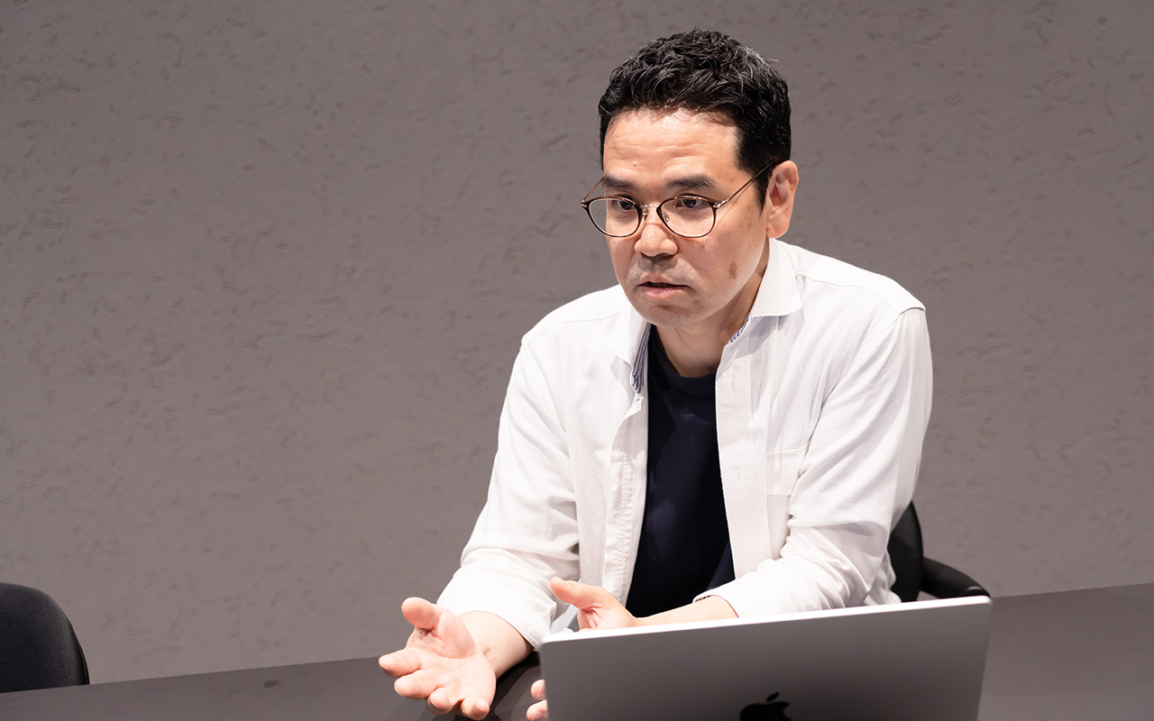 田中が両手を前に出して説明している様子