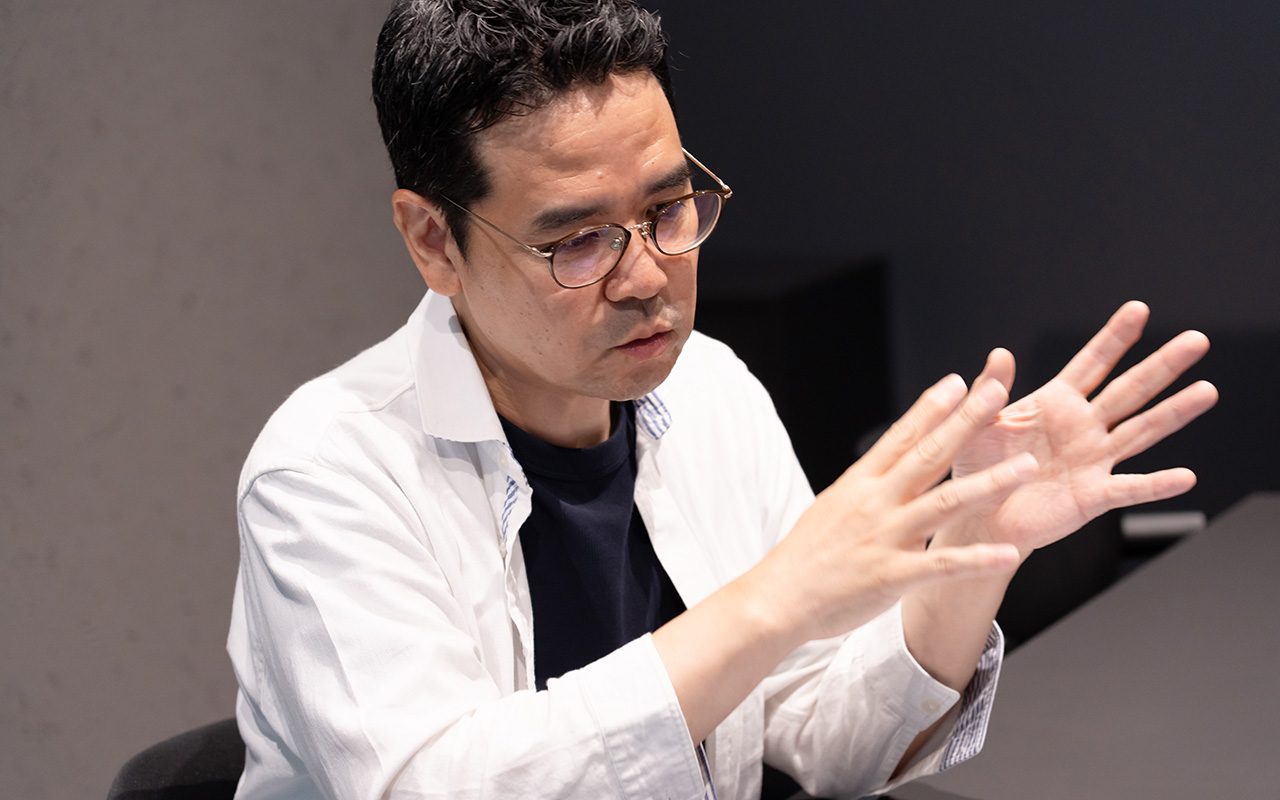 田中が両手を上げて説明している様子