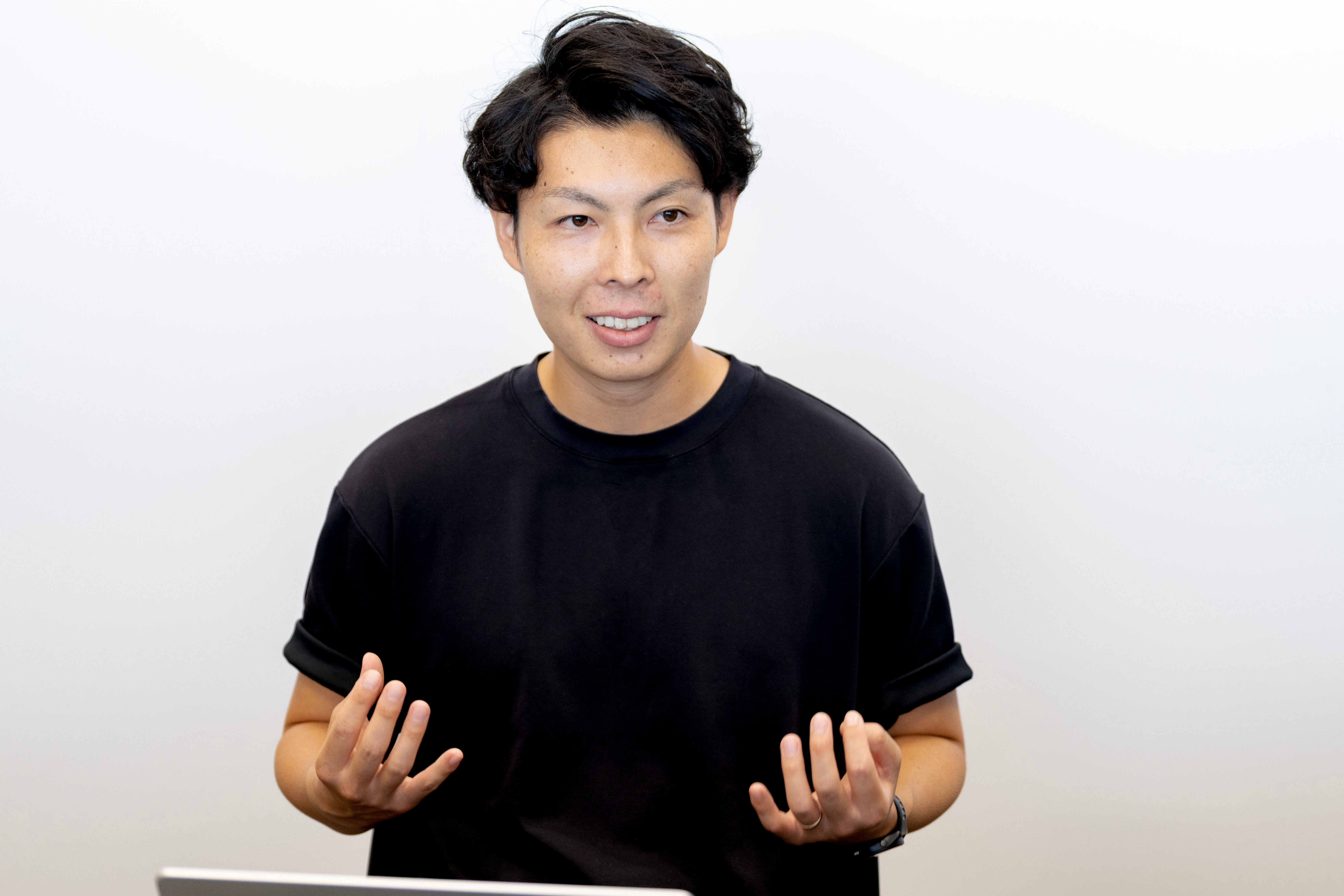 草田さんは、柔らかく自然な笑顔を浮かべ、両手を前に出して指を広げるジェスチャーをしながら話しています