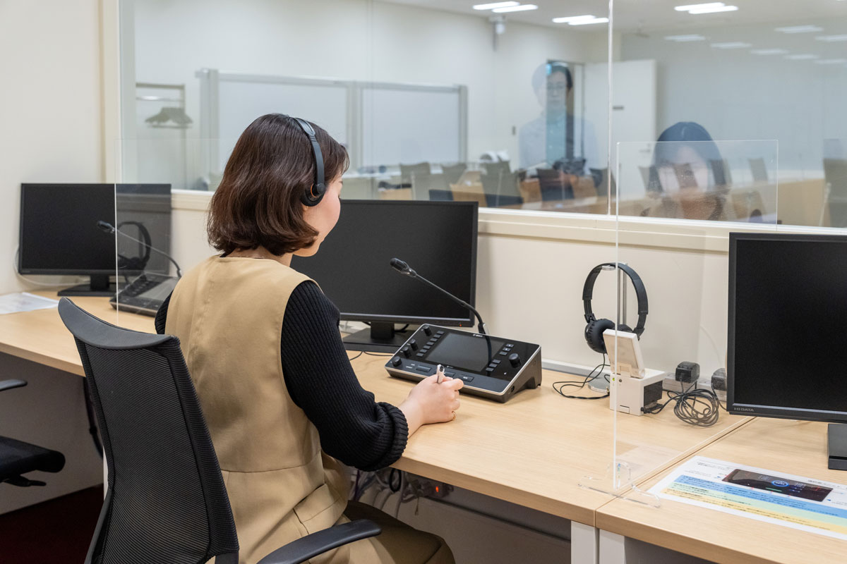 社内の大きめの会議室に確保されている通訳専用ブースの写真。渡部がデスクに向かい、通訳を再現。