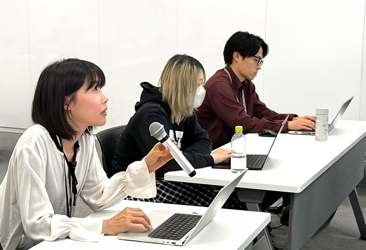 AIドラゴン桜プロジェクトでの授業風景。3名の生徒がパソコンを開き、1人の女性がマイクを持ち発表している