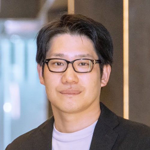 黒縁眼鏡をかけたリユース事業部責任者・林の上半身写真。黒いジャケットに淡い色のインナーを合わせ、落ち着いた表情でカメラを見つめている。背景には窓や木目調の壁が見える