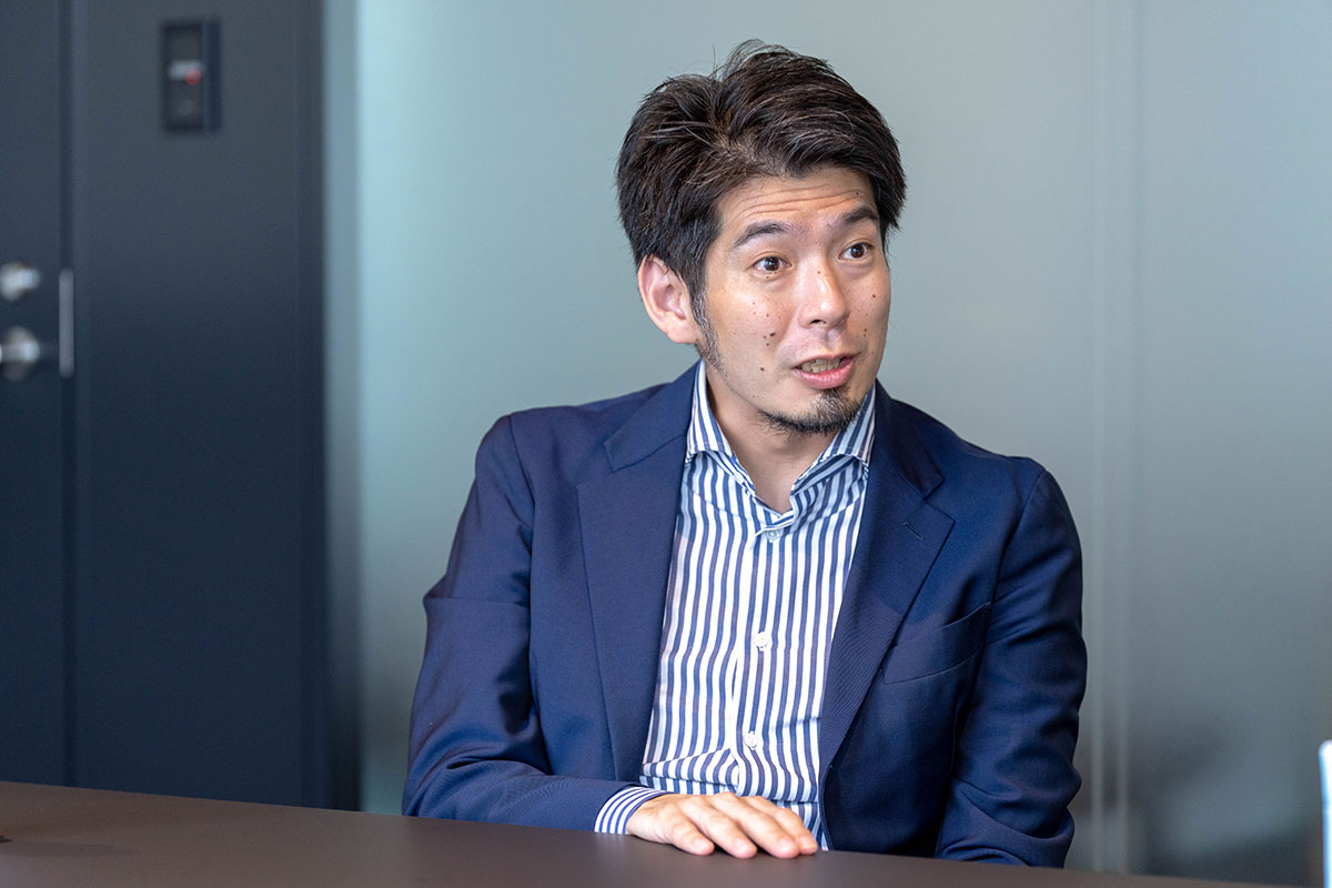 会議室で菅野先生がテーブルに手を置きながら話している写真。目を見開いて相手を見つめ、活発に議論している様子である。