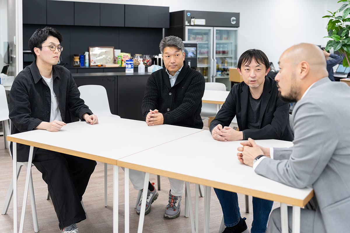 4人の男性がテーブルを囲んで真剣に話し合っている様子を写しています