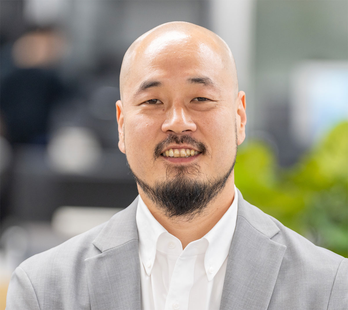 グレーのスーツを着た渡邊 誠さんのクローズアップです。彼はカメラに向かって微笑んでいます。