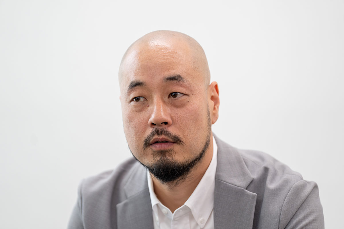 グレーのスーツを着た渡邊さんが真剣な表情で視線を横に向けている様子を捉えています