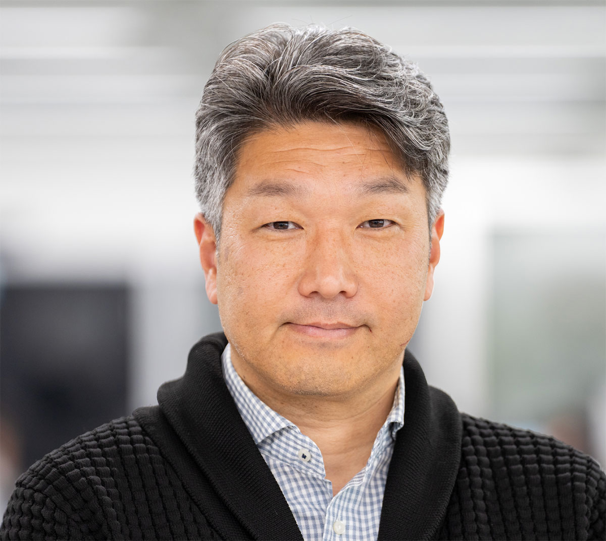 黒のカーディガンを着た福留進介のクローズアップです。落ち着いた表情でカメラを見ています。