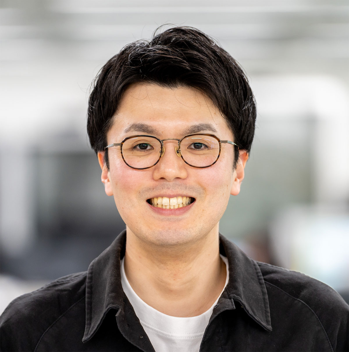 眼鏡をかけた亀岡千泰のクローズアップです。彼は明るく微笑んでいます。